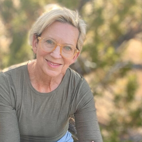 Roxanne Darling, Nature & Forest Therapy Guide portrait of roxanne darling, wearing glasses, sitting under a tree